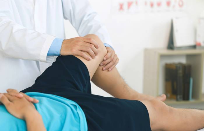 A doctor/physiotherapist checking the left knee of a patient lying on the bed.